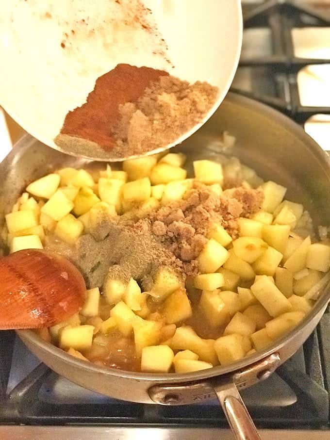 Spices being added to pan of cooking apples with wood spoon