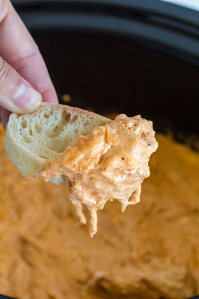Scooping Buffalo wing dip out of a crock-pot with a tortilla chip.