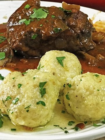 Serving of pork roast with three potato dumplings garnished with parsley.