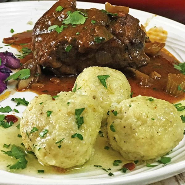 Serving of pork roast with three potato dumplings garnished with parsley.