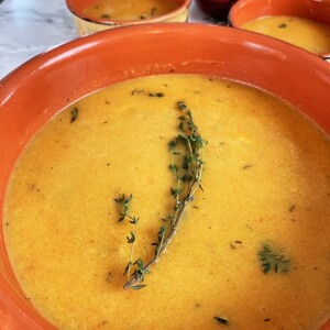 A bowl of butternut squash soup in an orange bowl with fresh rosemary garnish