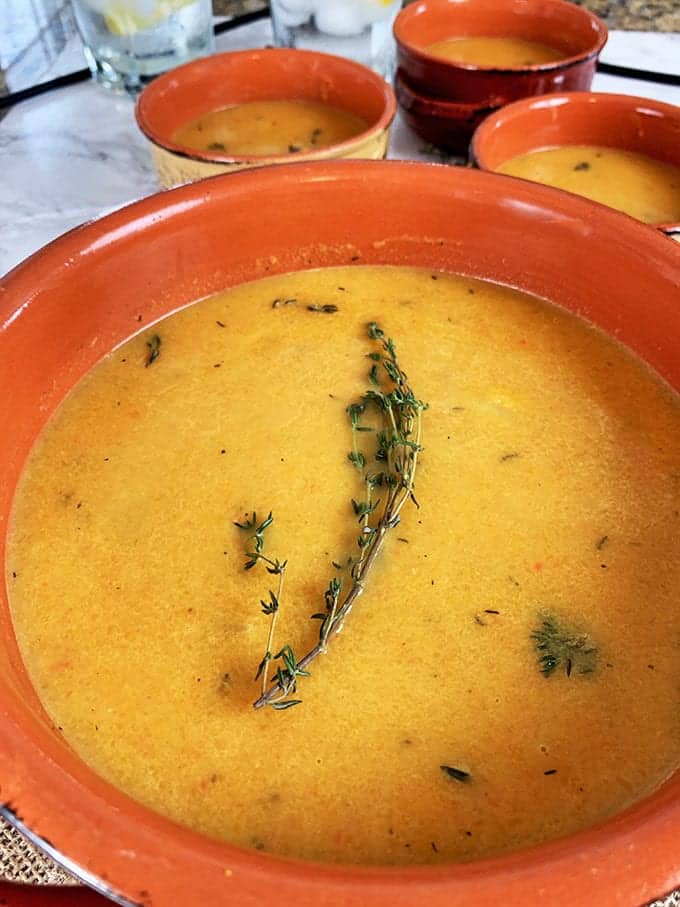 A bowl of butternut squash soup in an orange bowl with fresh rosemary garnish