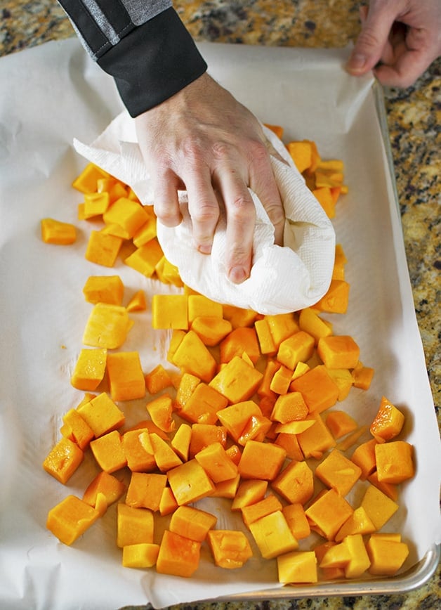 A hand holding a paper towel to blot moisture from butternut squash