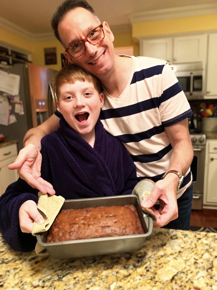 teenage boy holding a loaf of homemade banana bread with his father.