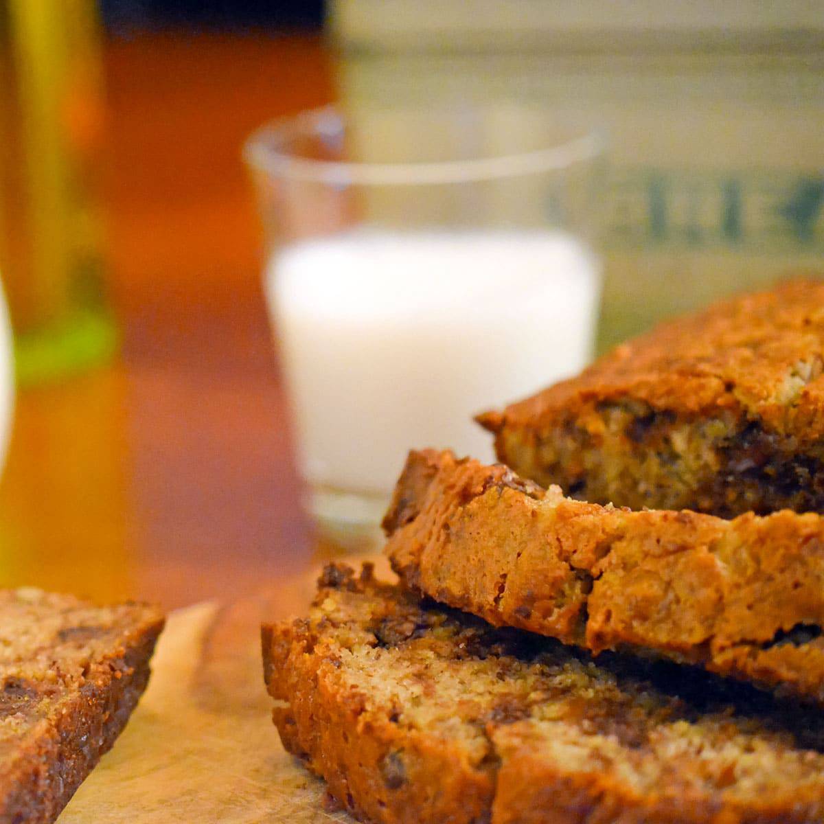 Sliced loaf of banana breqd in front of a glass of milk.