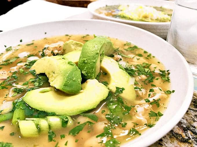 A bowl of soup with slices of avocado on top