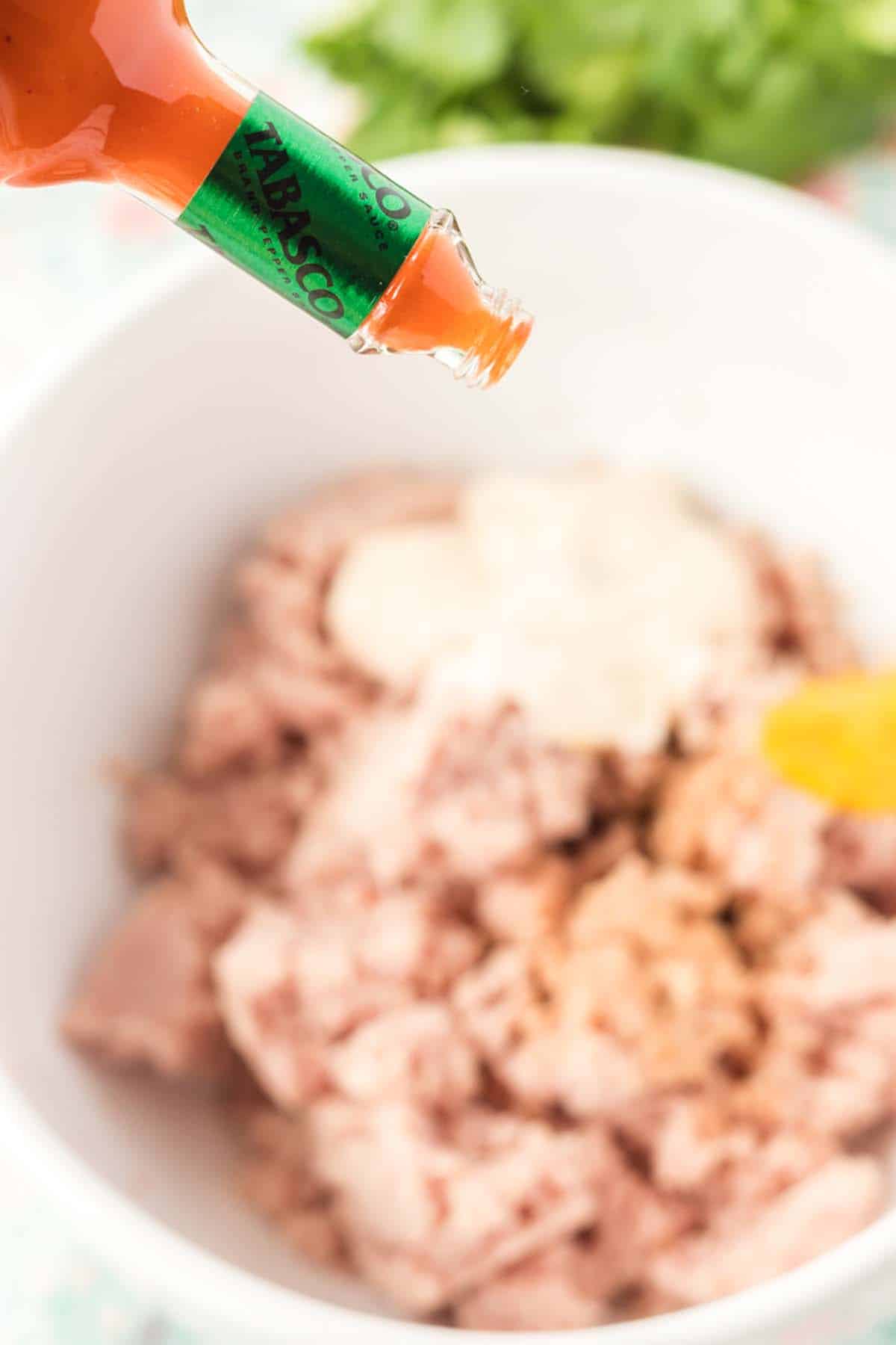 Adding some hot sauce to a bowl of deviled ham mixture.