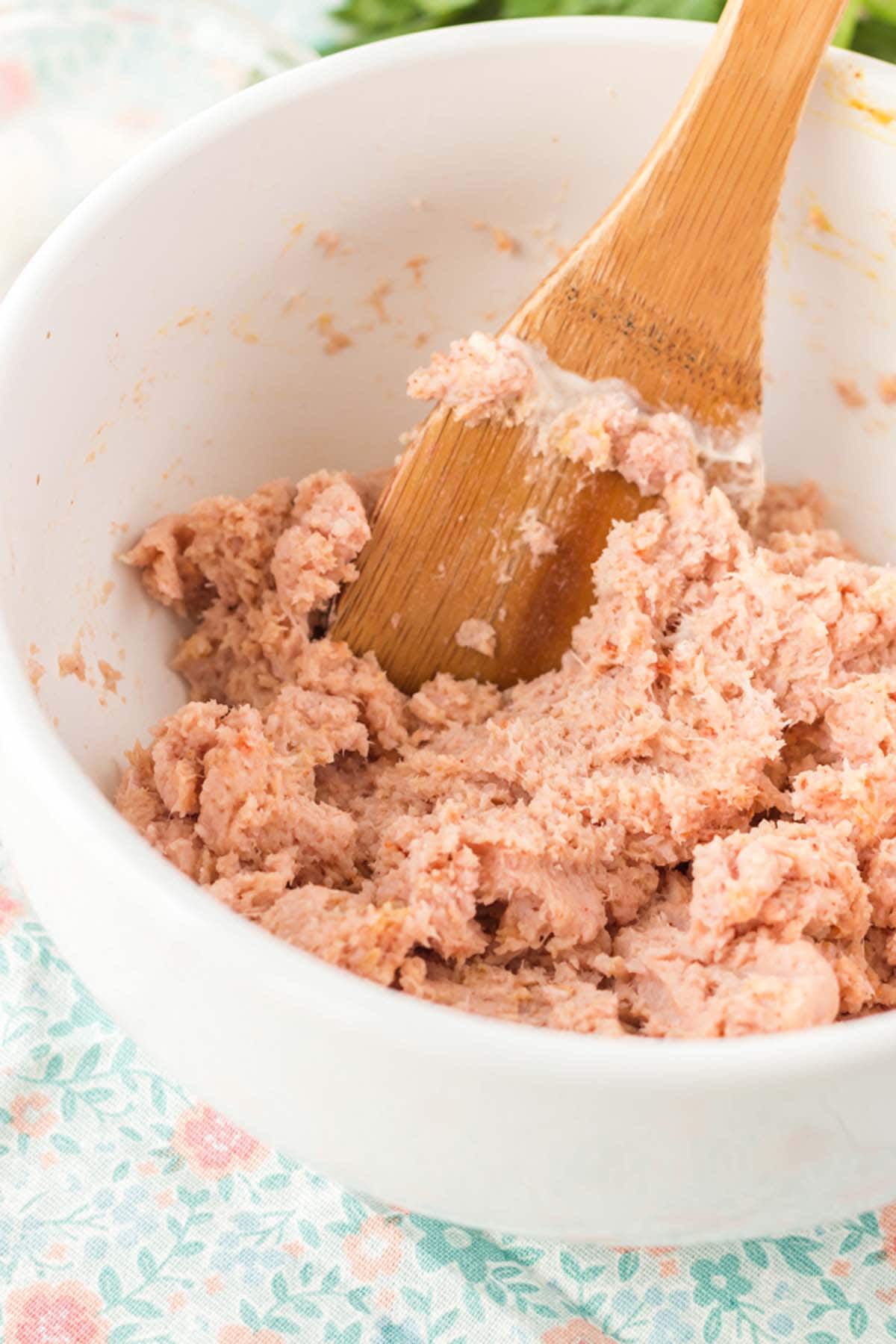 A wooden spoon in a bowl of ham salad.