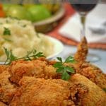 Serving plate of oven-fried chicken with mashed potatoes and a glass of red wine.