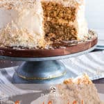 Slice of coconut carrot cake with full cake in background.