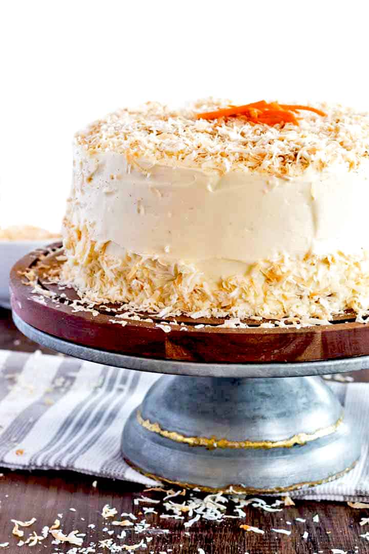 homemade carrot cake on a pedistal with toasted coconut cream cheese frosting.