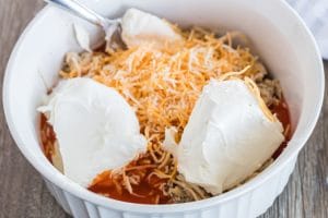 Mixing bowl with cream cheese, shredded cheese, hot wing sauce, and shredded chicken.
