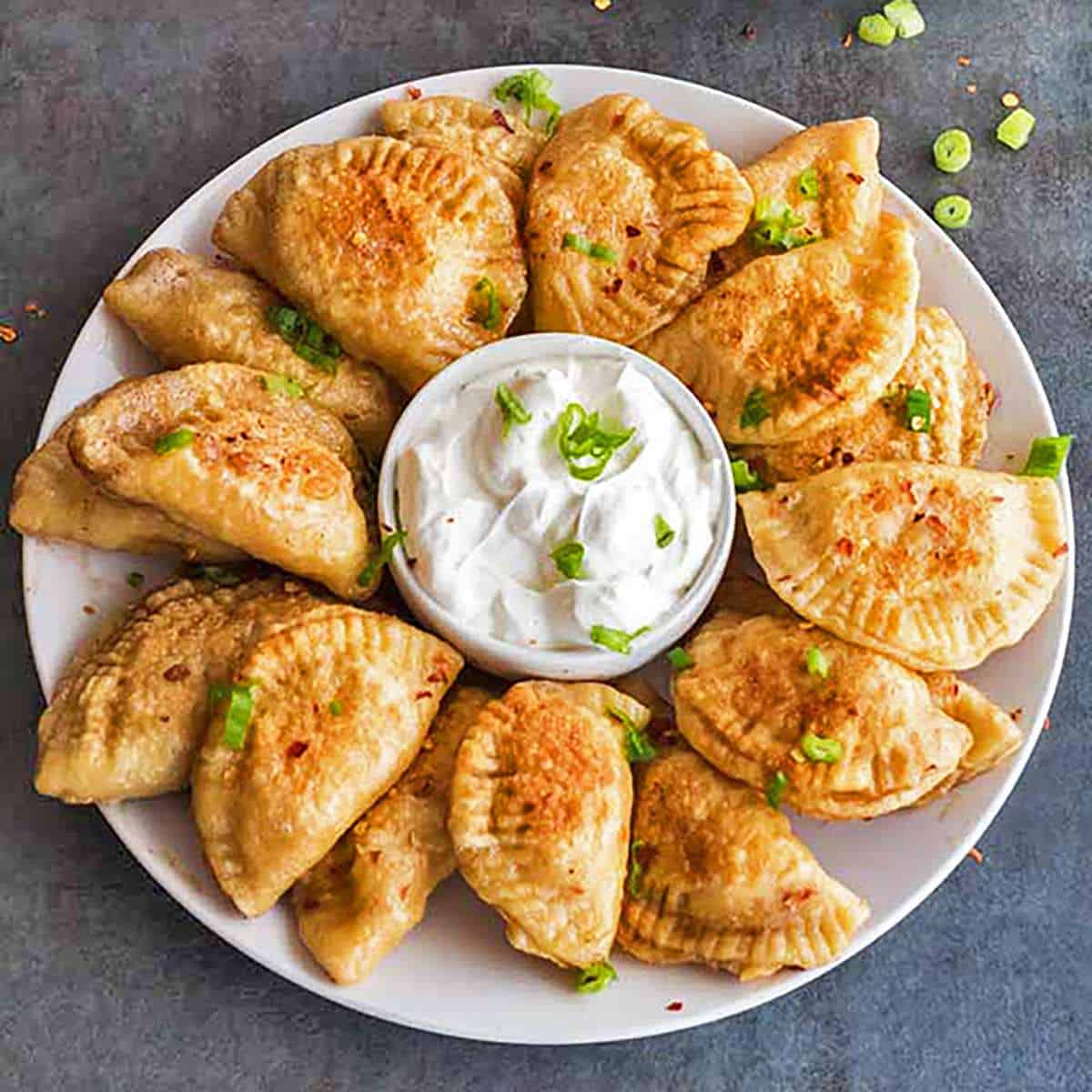 Round plate of pierogi with sour cream in the center.