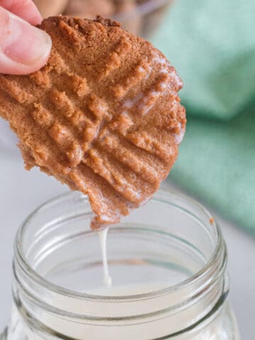 A peanut butter cookie being dunked in milk.