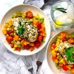 Two bowls of summer succotash topped with chicken breast and a glass of ice water.