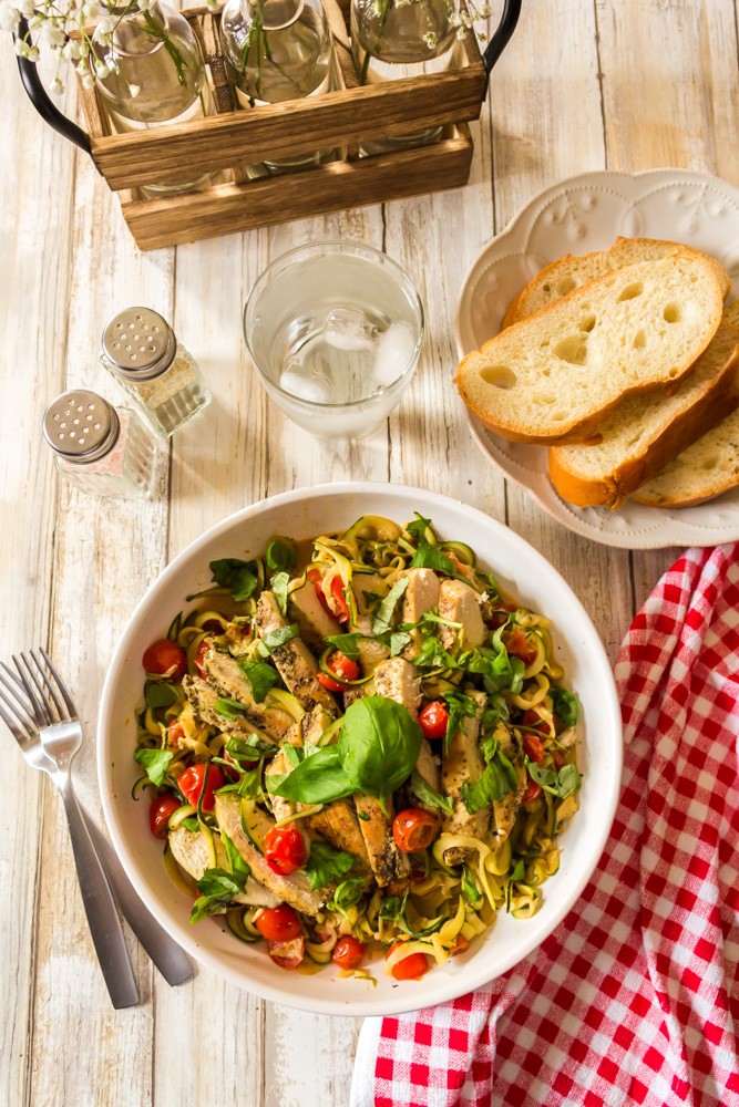 A serving of veggie noodles and chicien. A plate of food with a side dish of bread.