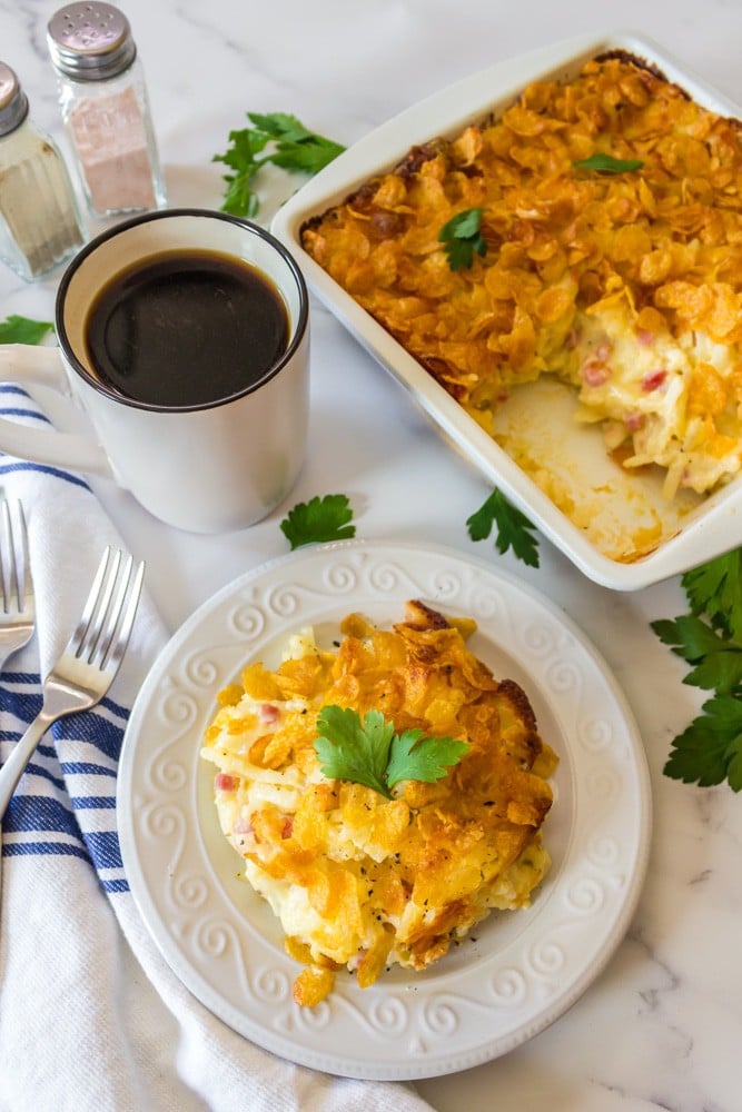 Serving of cheesy hashbrown casserole with cup of coffee.