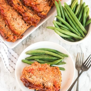 Platter of metloaf cut into portions with green beans on the side.