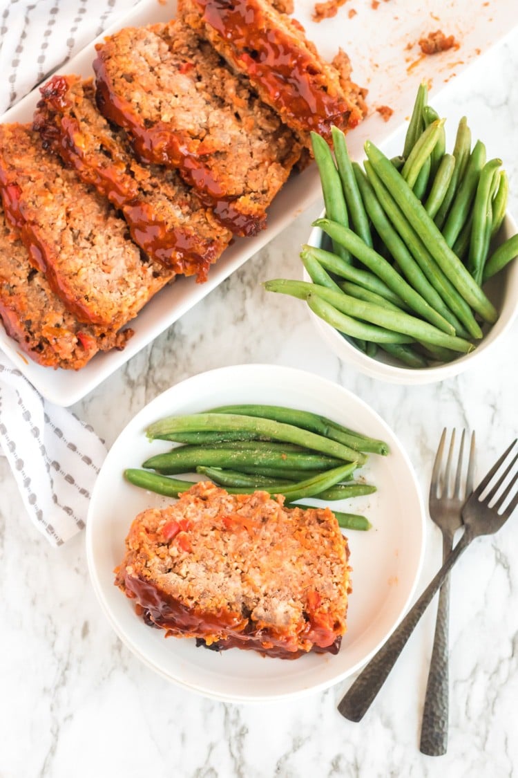 Platter of metloaf cut into portions with green beans on the side.