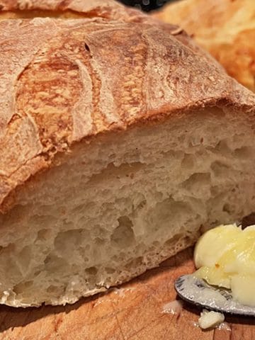 Cut loaf of crusty bread with butter and butter knife.