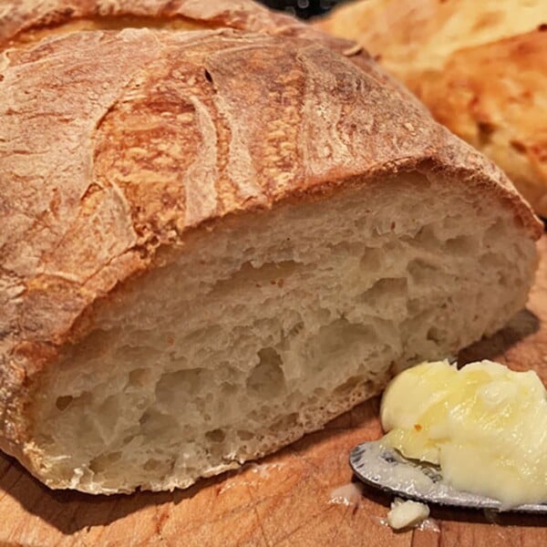 Cut loaf of crusty bread with butter and butter knife.