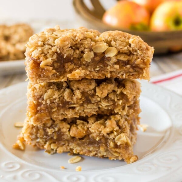 stack of three oatmeal dessert bars with appeles in the background,.