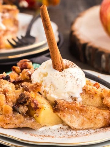 Dutch apple pie on a plate with ice cream and a cinnaomn stick.