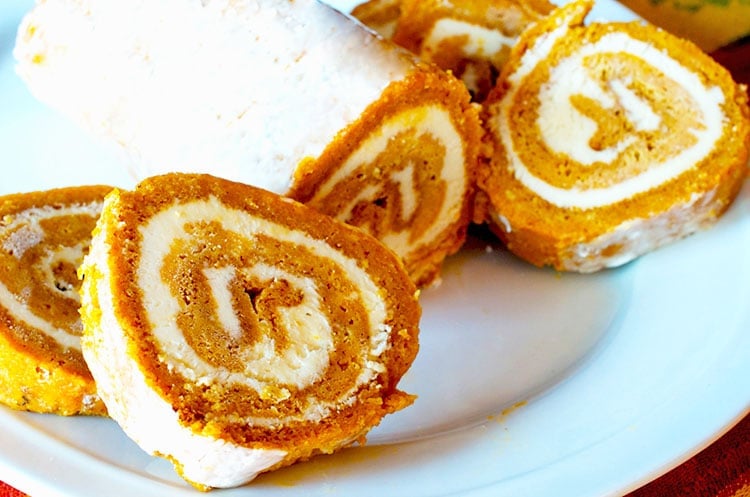 Pumpkin roll on a white seviong platter with four slices carved.