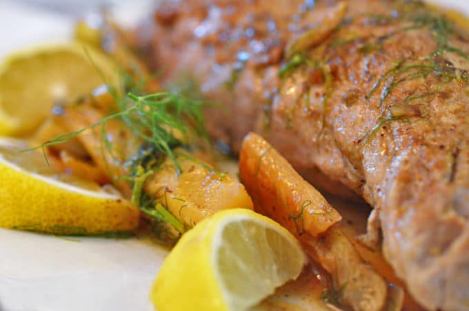 Pork tenderloin with garnishes of fennel and garlic and a lemon wedge.