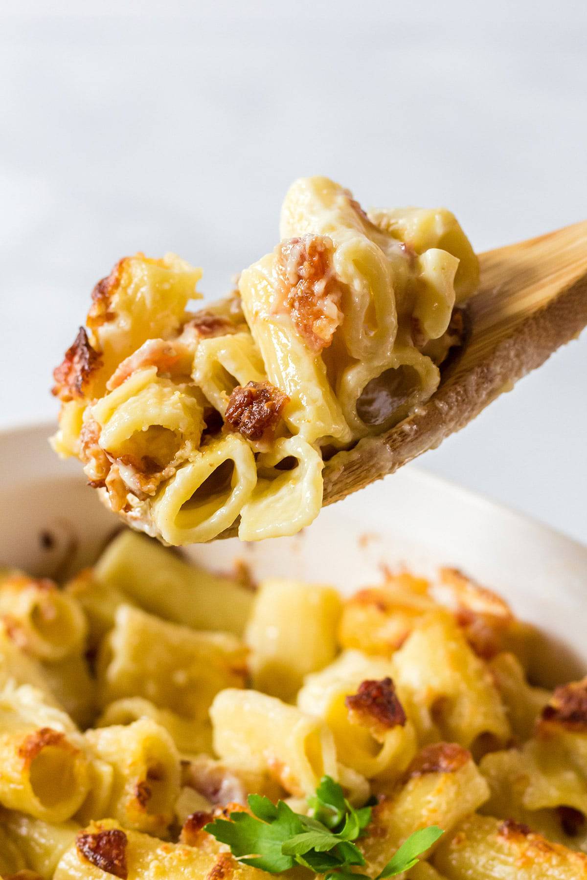 Wooden spoon scooping out bacon mac and cheese from a pan.