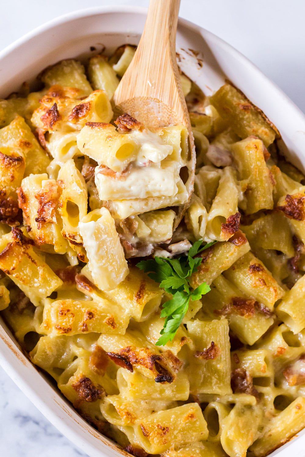 Scooping out baked mac and cheese from a 2-quart baking dish, using a wooden spoon.