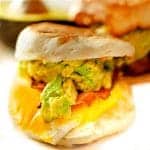 English muffin breakfast sandwich with avocado and cheddar cheese oozing out.