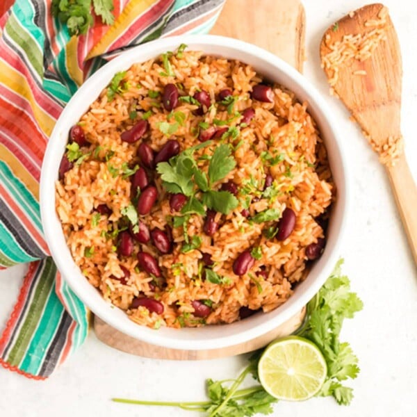 Bowl of Spanish rice and beans with a lime and wooden spoon on the side.