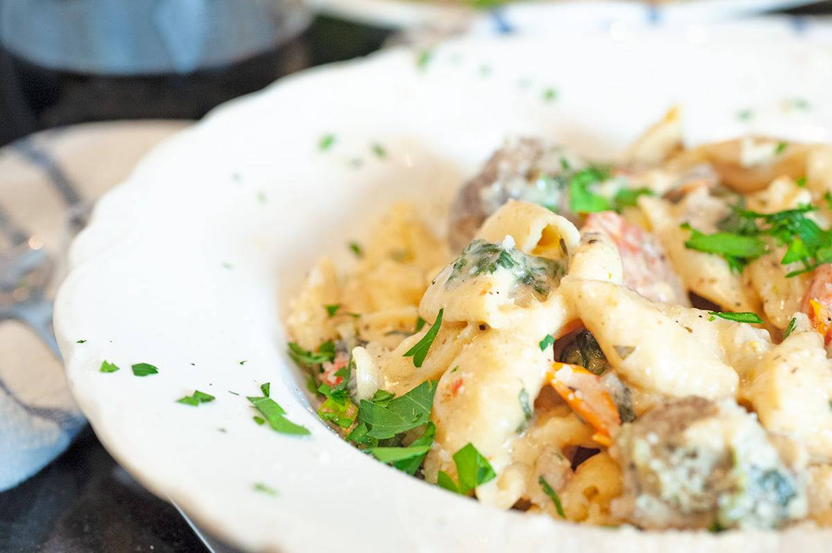 Serving plate of creamy pasta and sausage, garnished with parsley.