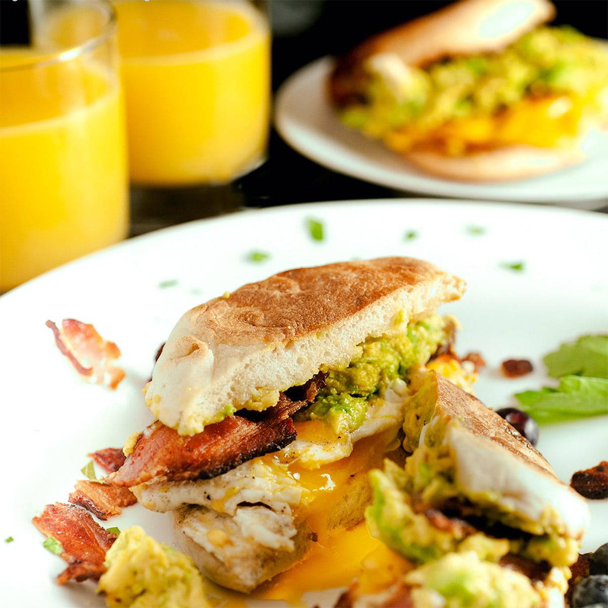 Avocado breakfast muffin cut in half with glasses of orange juice in the background.