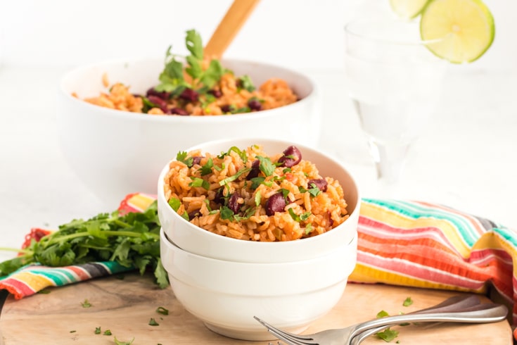 White bowl of Spanish rice and beans with serving bowl in the background.