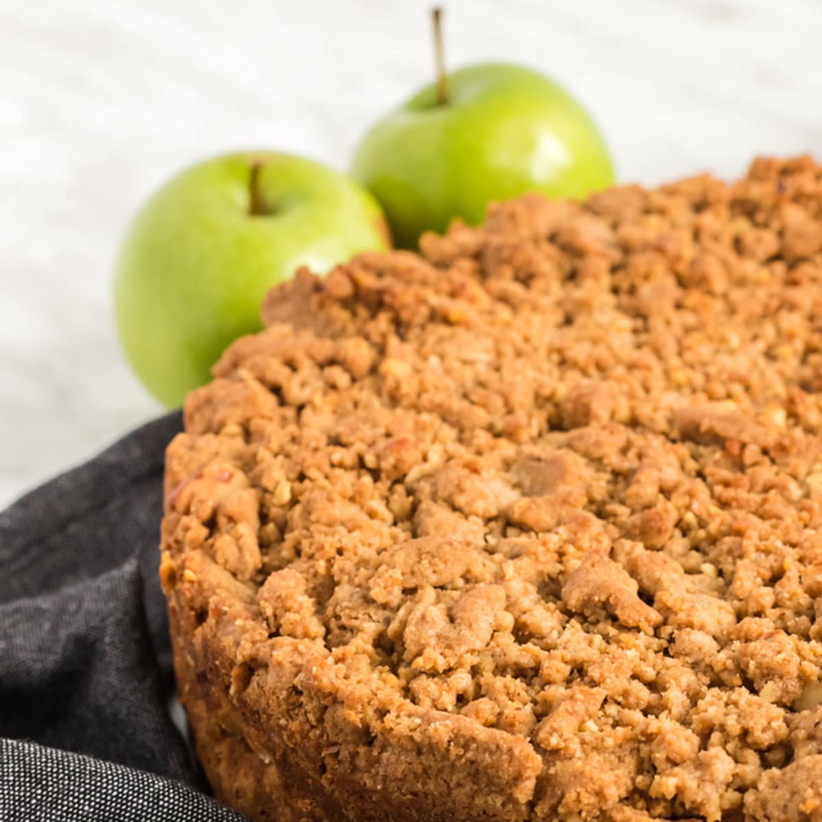 A cake topped with a crumb topping and two Ganny Smith apples