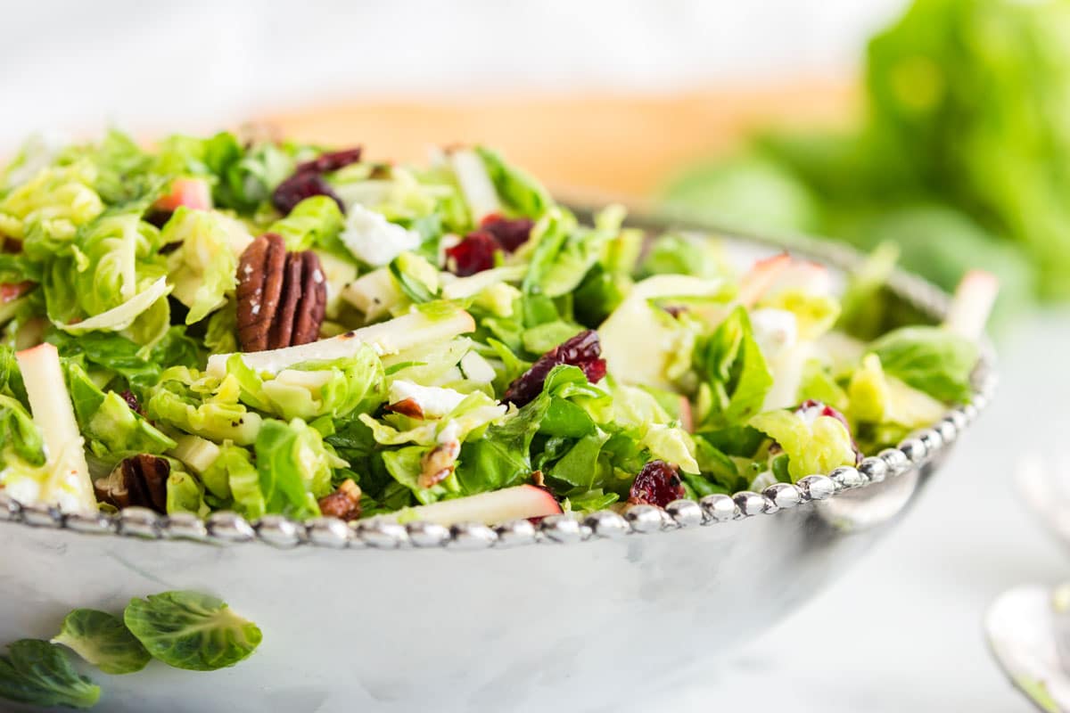 A bowl with green salad and pecans and apples.