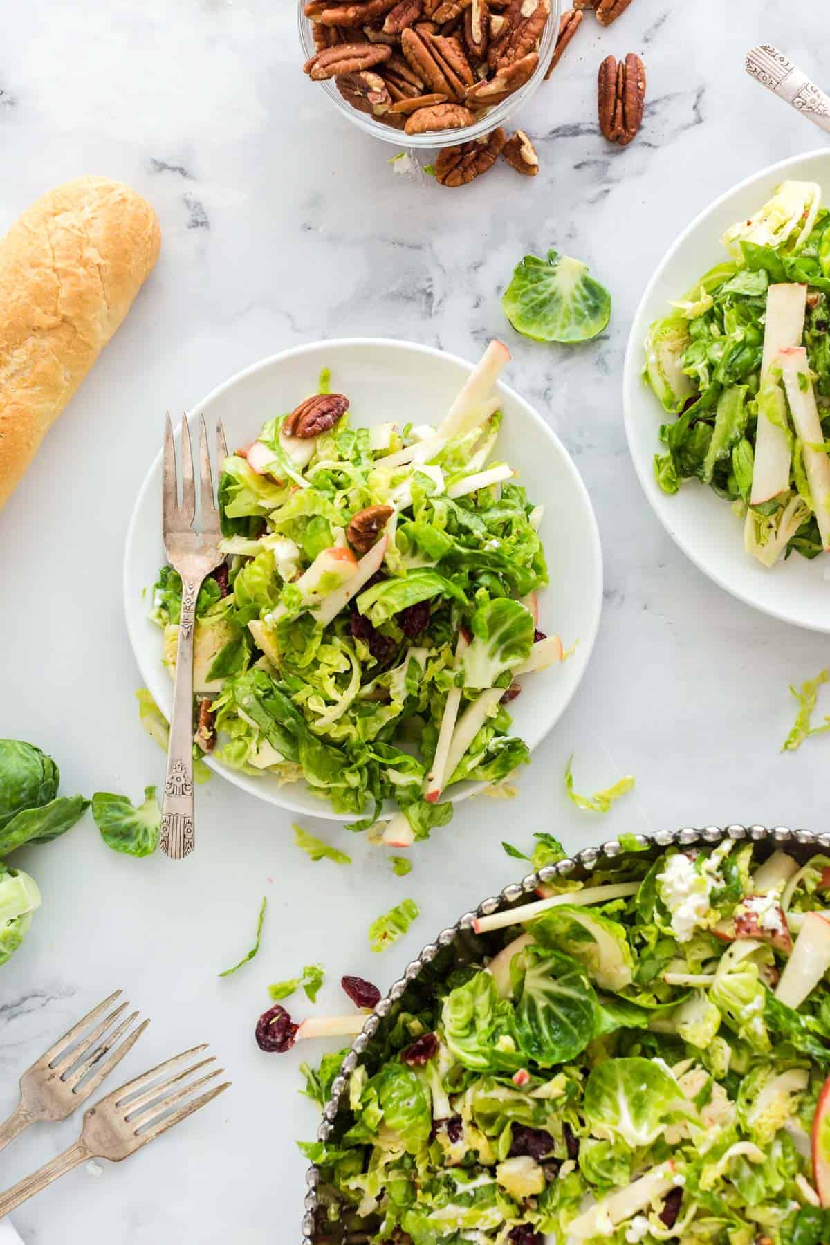 Three bowls of Brussels sprouts salad with walnuts and a baguette of bread