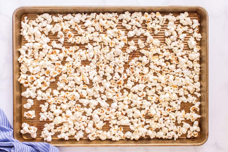 Single layer of popcorn on a rimmed baking sheet.