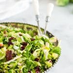 A bowl of green salad with kitchn tongs and bread