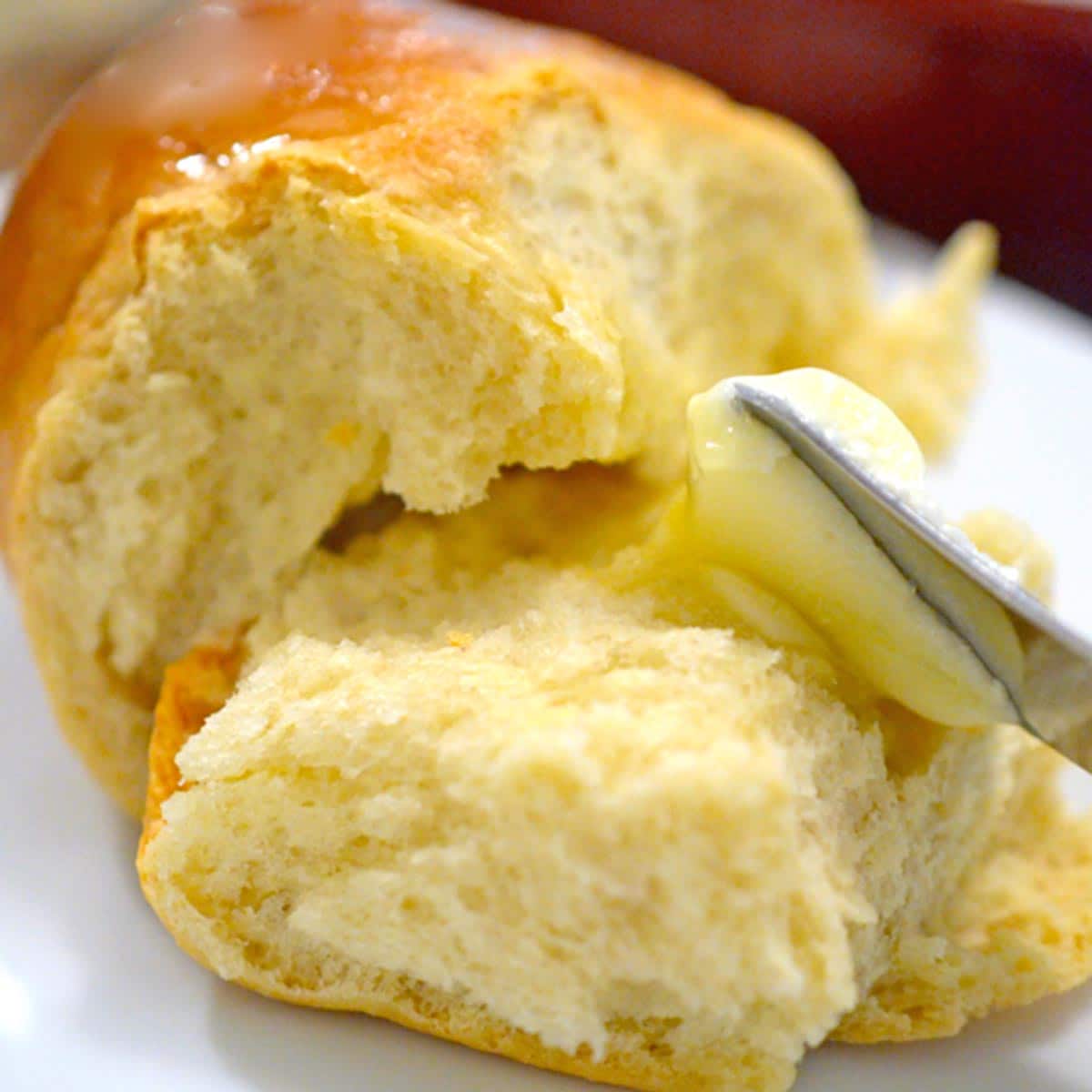 A dinner roll being buttered.