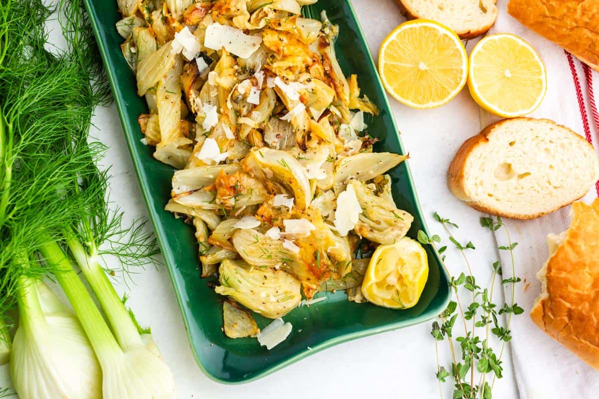 A tray of roasted fennel with a baguette of bread and fresh oregano