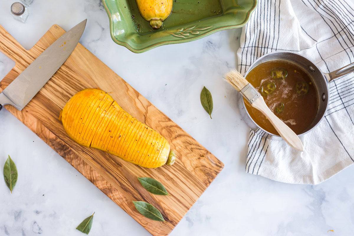Glazing a hasselback butternut squash A squash on a cutting board with a pan of sauce