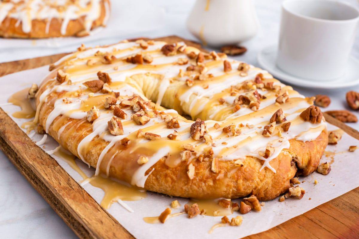 Danish kringle with pecan filling A Danish kringle on a cutting board with nuts and frosting.