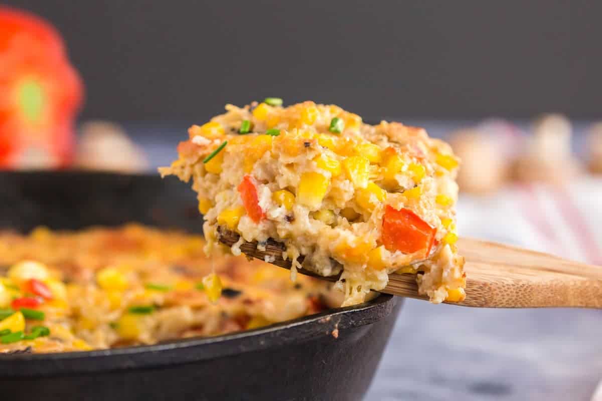 A portion of corn casserole. A scoop of scalloped corn on a wooden spoon.