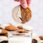 a hand dunking a cookie in a glass of milk