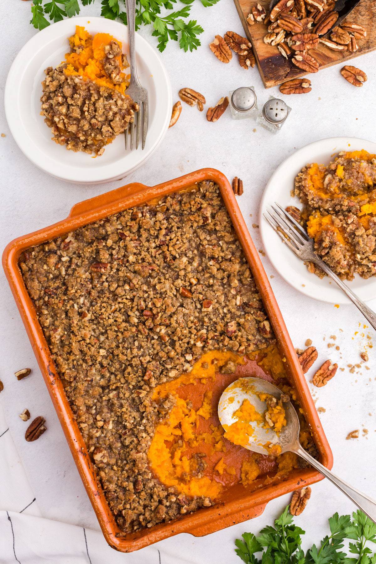 A casserole with two plates and scattered pecans.