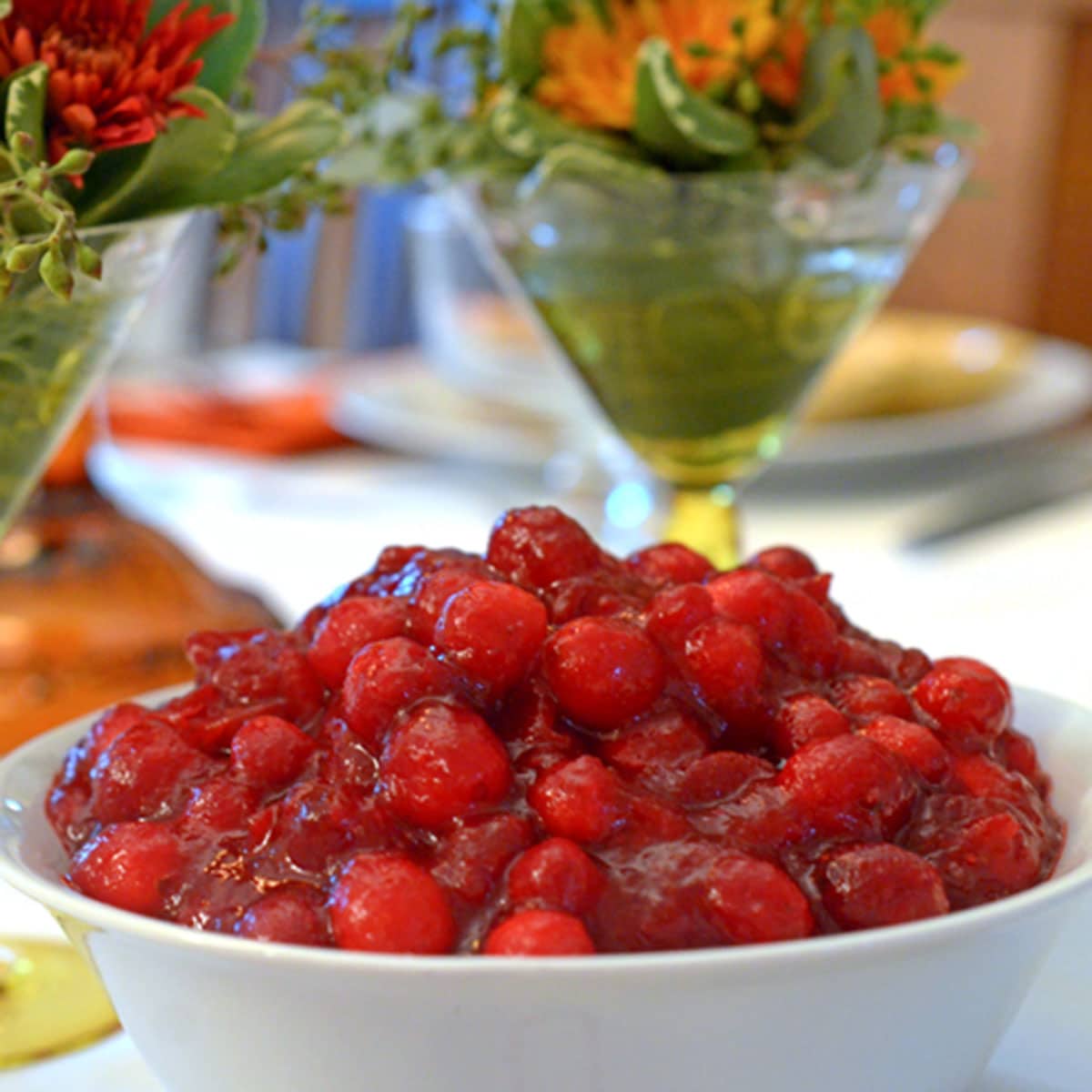 A bowl of cranberries with flower arrangement in background