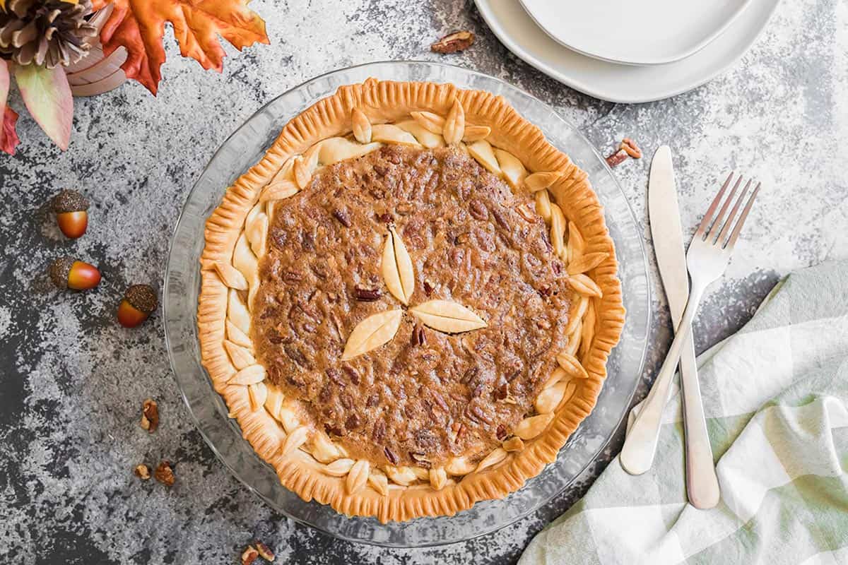 A homemade pie with acorns and fall leaves on the side.